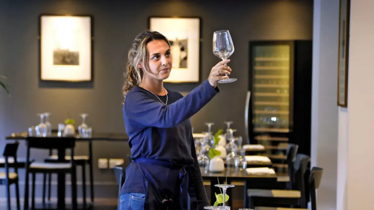 A young waiter inspects a glass in a restaurant