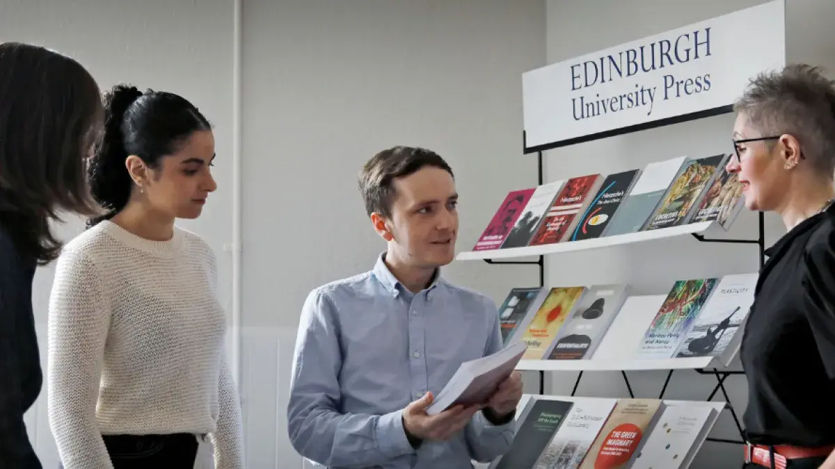 A group of EUP colleagues stand in conversation around a stack of books