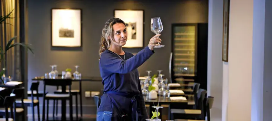 A young waiter inspects a glass in a restaurant