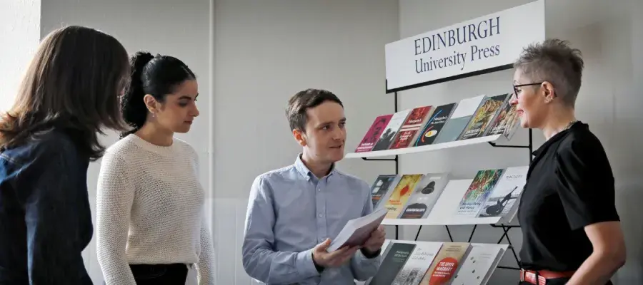 A group of EUP colleagues stand in conversation around a stack of books