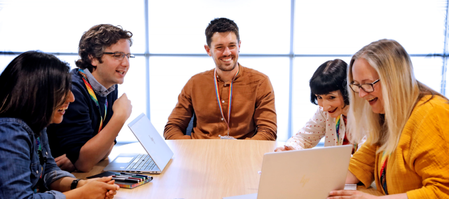 Five colleagues from HR look at a laptop smiling 