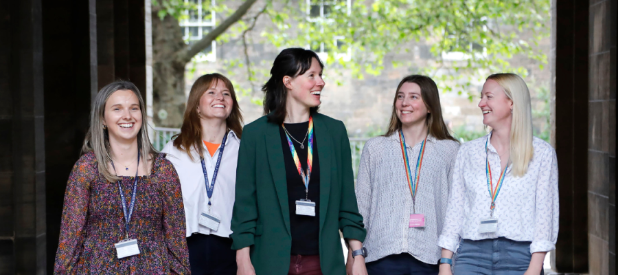 A group of five female colleagues walk and talk outside