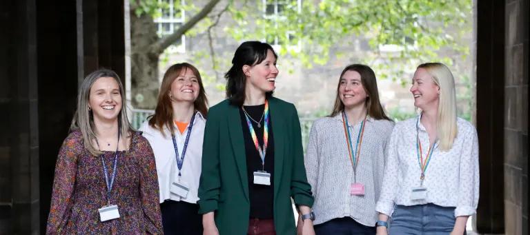 A group of five female colleagues walk and talk outside