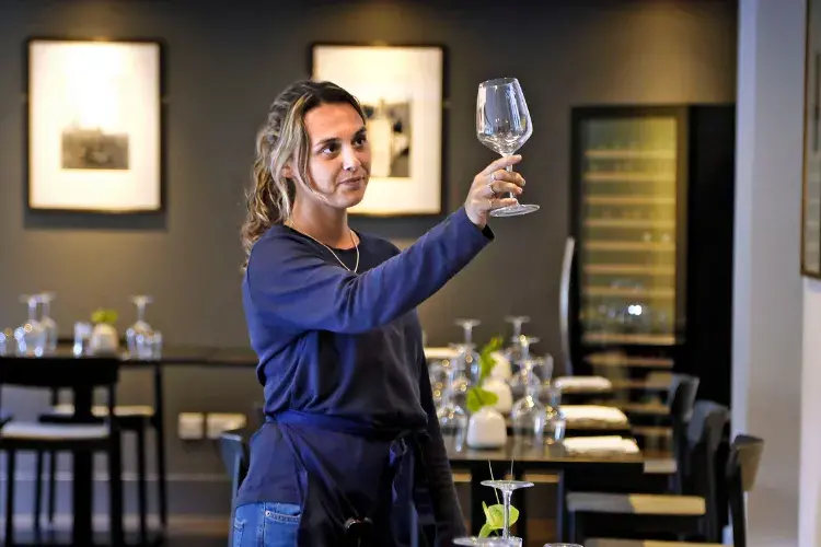 A young waiter inspects a glass in a restaurant
