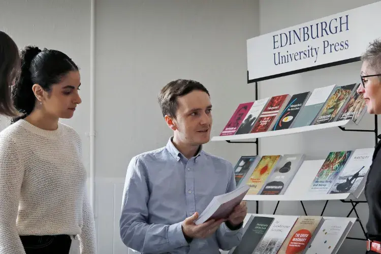 A group of EUP colleagues stand in conversation around a stack of books