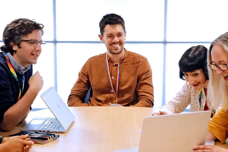 Five colleagues from HR look at a laptop smiling 