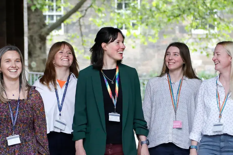 A group of five female colleagues walk and talk outside