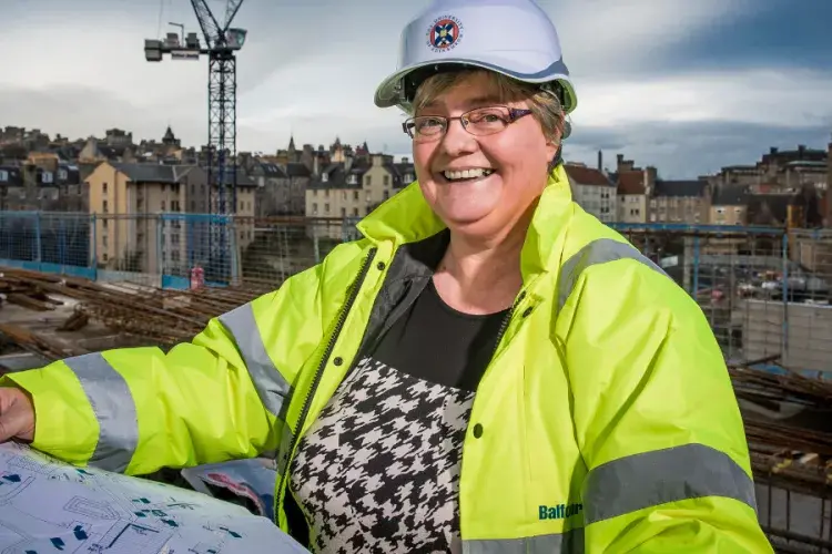 An Estates deputy director holds out plans while wearing a hi-vis jacket